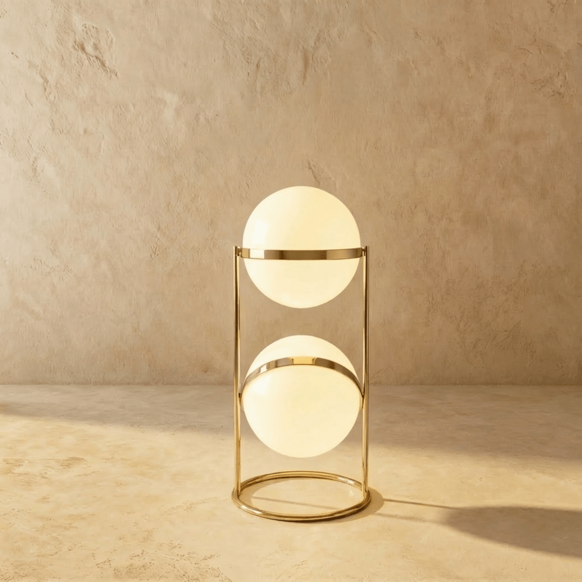 Clérachic two-globe sphere lamp in polished brass, the short column lit against a plaster studio wall.