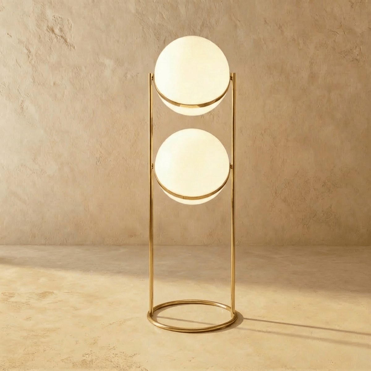 Clérachic two-globe sphere lamp in polished brass on the taller column, both globes lit against a seamless plaster backdrop.