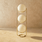 Clérachic three-globe sphere lamp in polished brass, shown unlit, each white globe shaded and marked by a specular highlight.