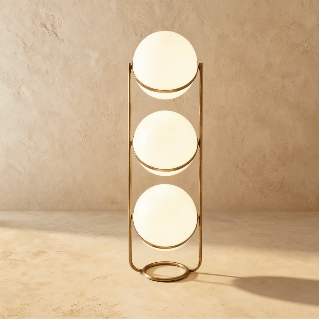 Clérachic three-globe sphere lamp in vintage brass, lit, standing on the sandy plaster studio backdrop.