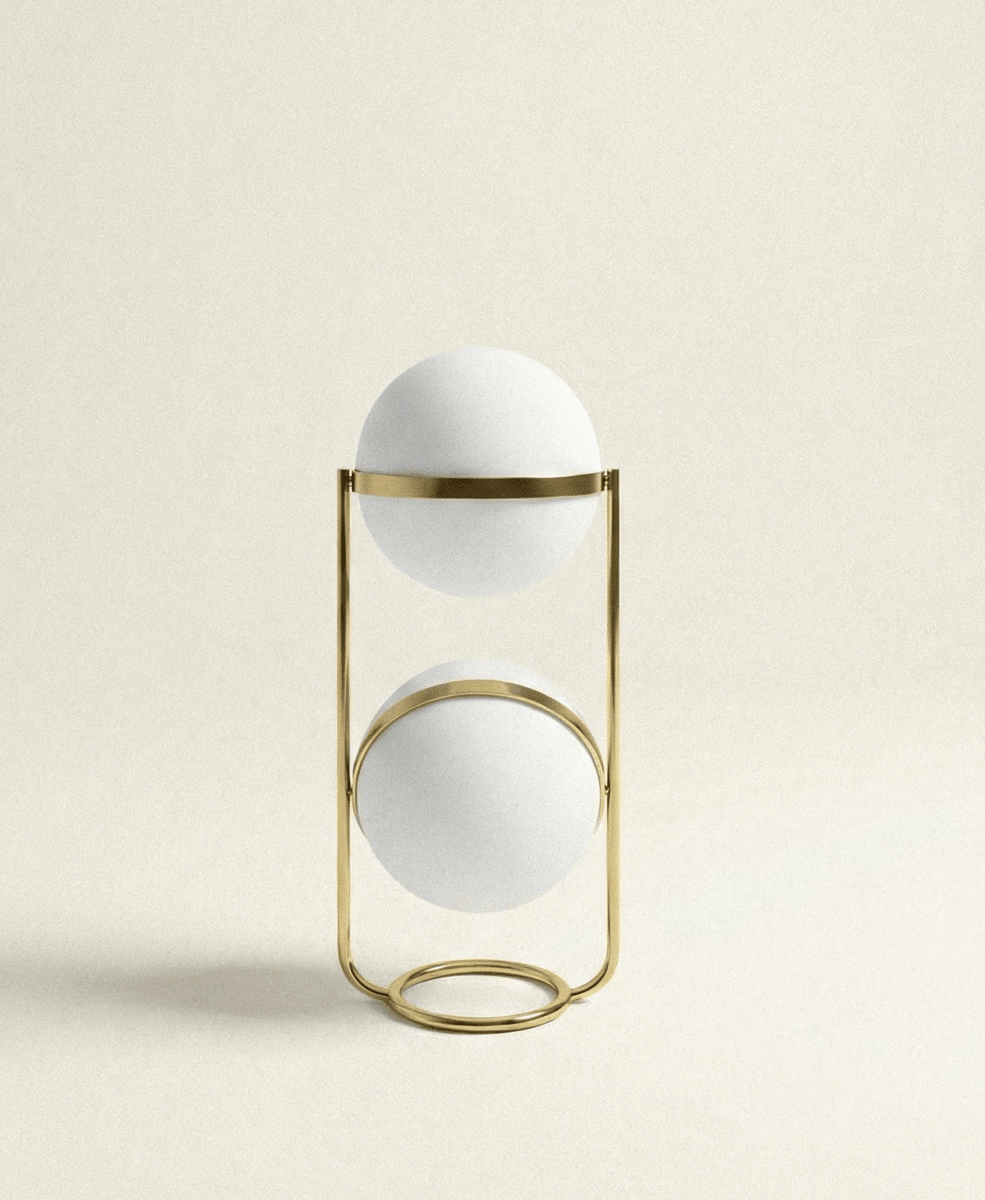Clérachic two-globe sphere lamp in brass, unlit on a plain cream ground, the upper band mid-way up its globe and the lower band near the top of its own.
