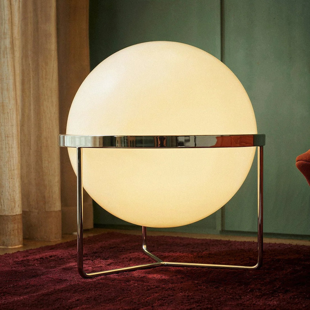 Clérachic single-globe sphere lamp standing on a deep red rug, its mirror-polished band reflecting the green panelled wall behind it.