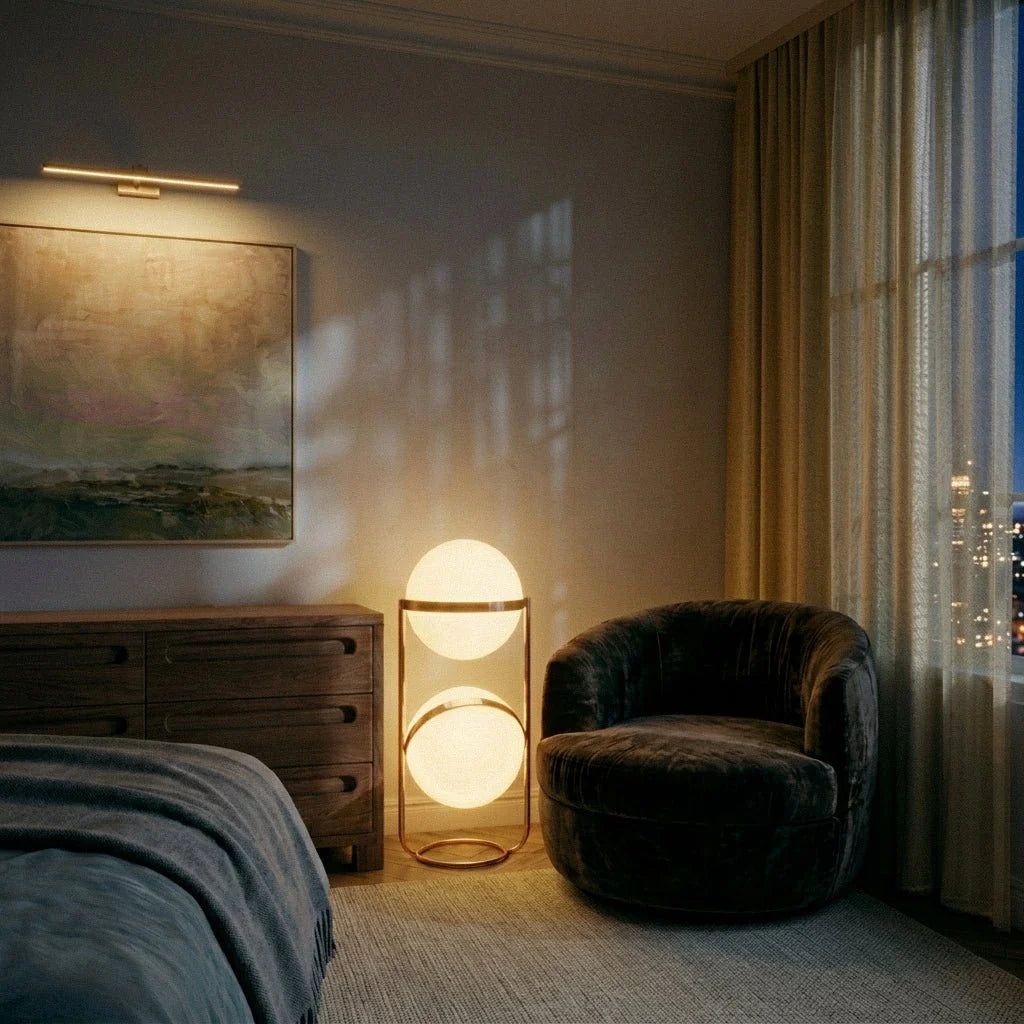 Clérachic two-globe sphere lamp in brass, lit at floor level in a bedroom beside a dark velvet swivel chair and a night skyline.