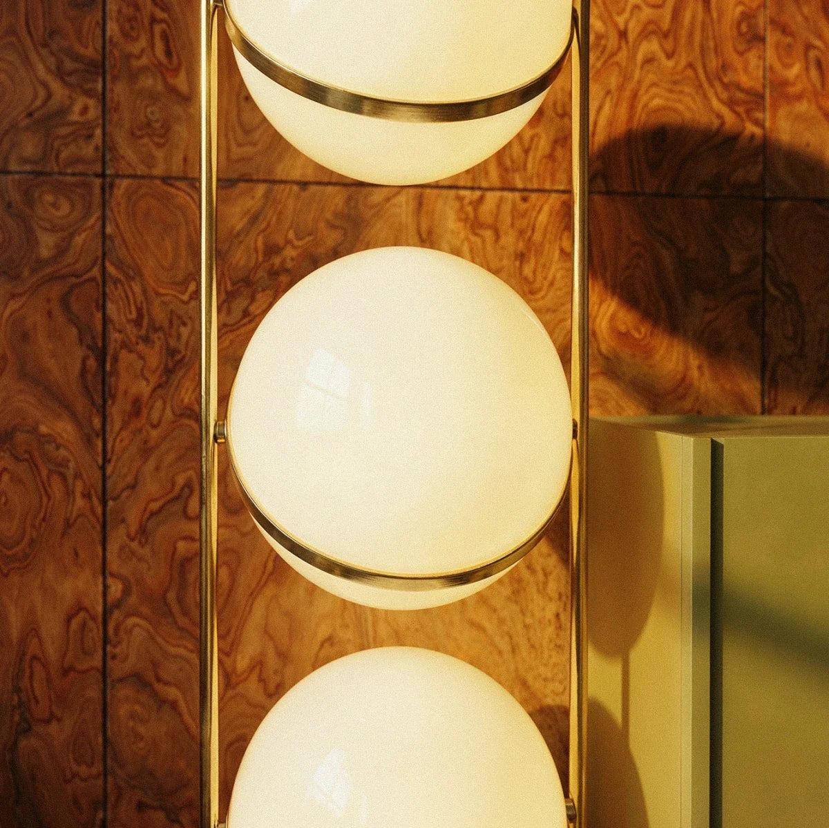 Clérachic three-globe sphere lamp in brass, a close crop of the middle globe and its band against the burl-wood panelling.