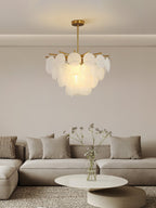 A Clérachic frosted glass disc chandelier glowing over a cream sofa and a low round coffee table with a vase of stems.