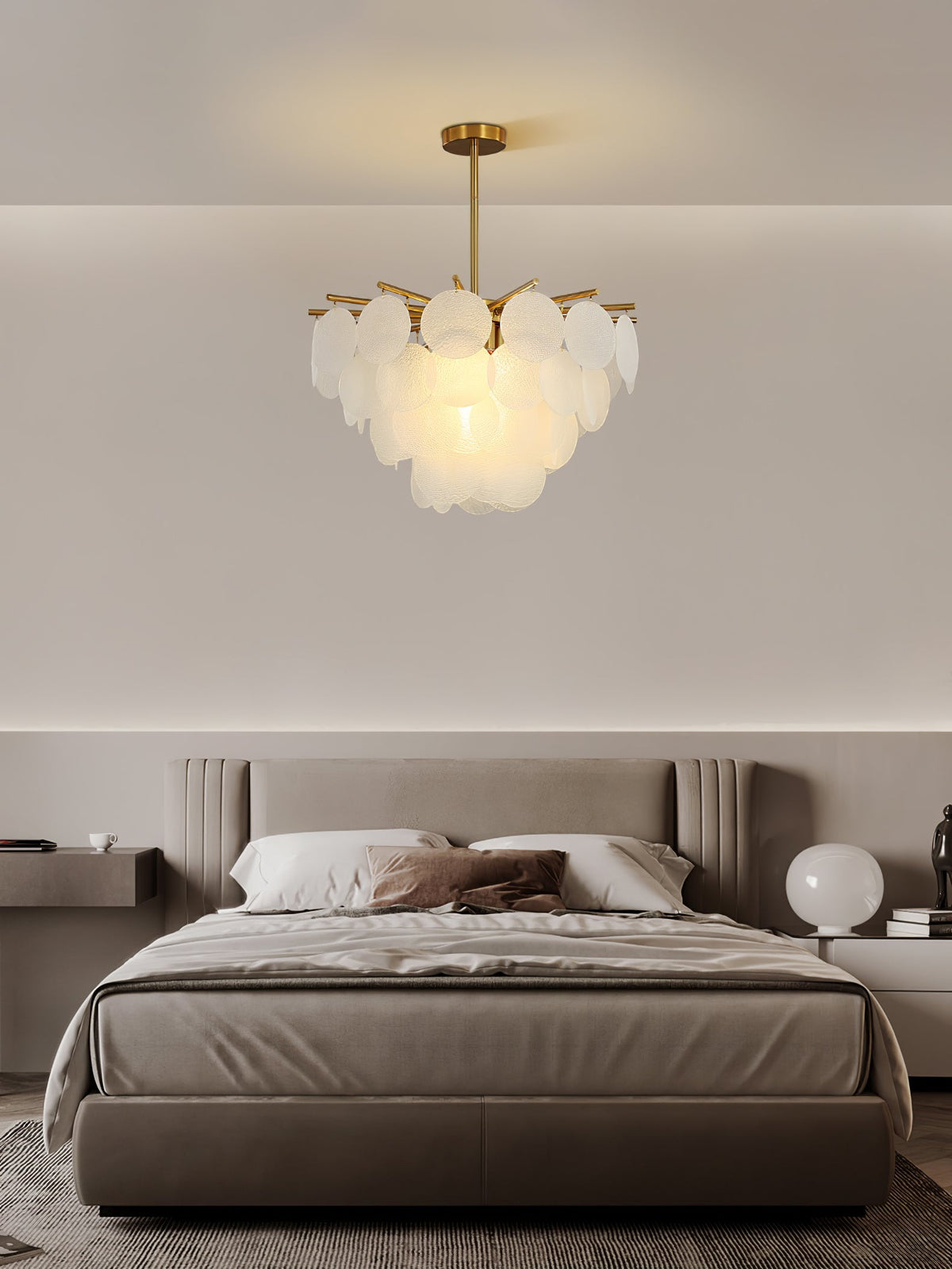 Compact Clérachic chandelier of layered glass discs, hung in a calm taupe bedroom above a bed with soft grey bedding.