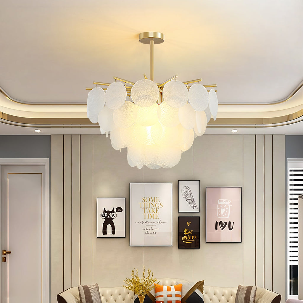 Frosted glass discs on a gold-toned frame, this Clérachic chandelier lit beneath a curved ceiling with framed prints behind.