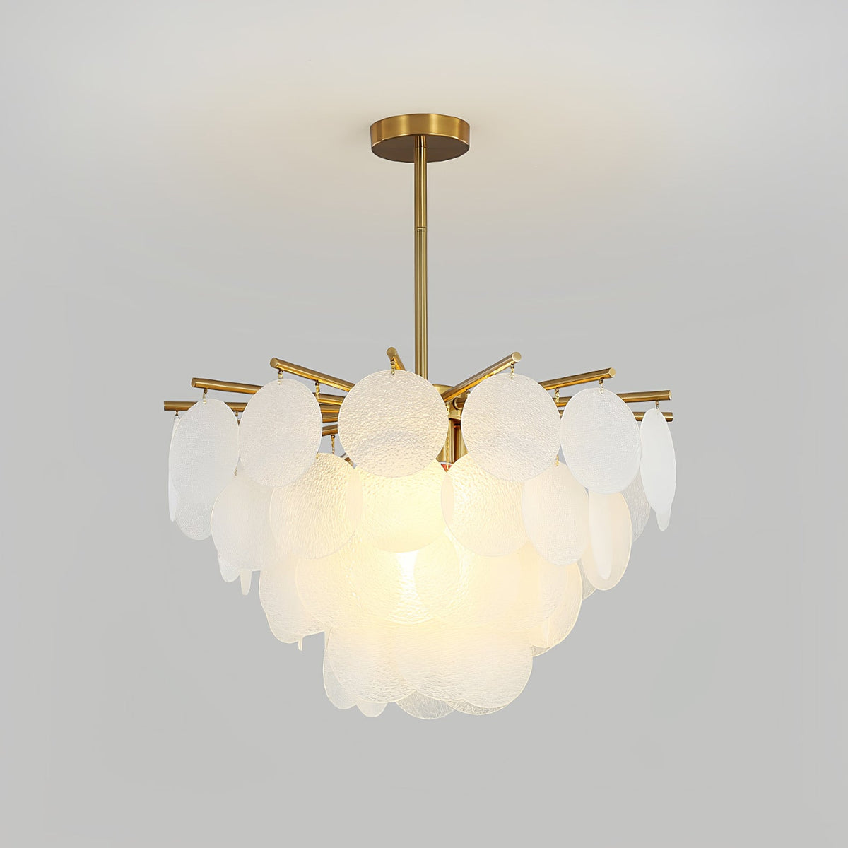 Close, lit view of the layered frosted discs and brass-toned arms of this Clérachic chandelier against a pale grey wall.