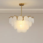 The upper tier of round textured discs and brass arms on this Clérachic chandelier, lit warmly, in a plain pale room.