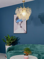 Close crop of this Clérachic chandelier, lit amber-white, hanging before a blue wall and a framed portrait with a blue brushstroke.
