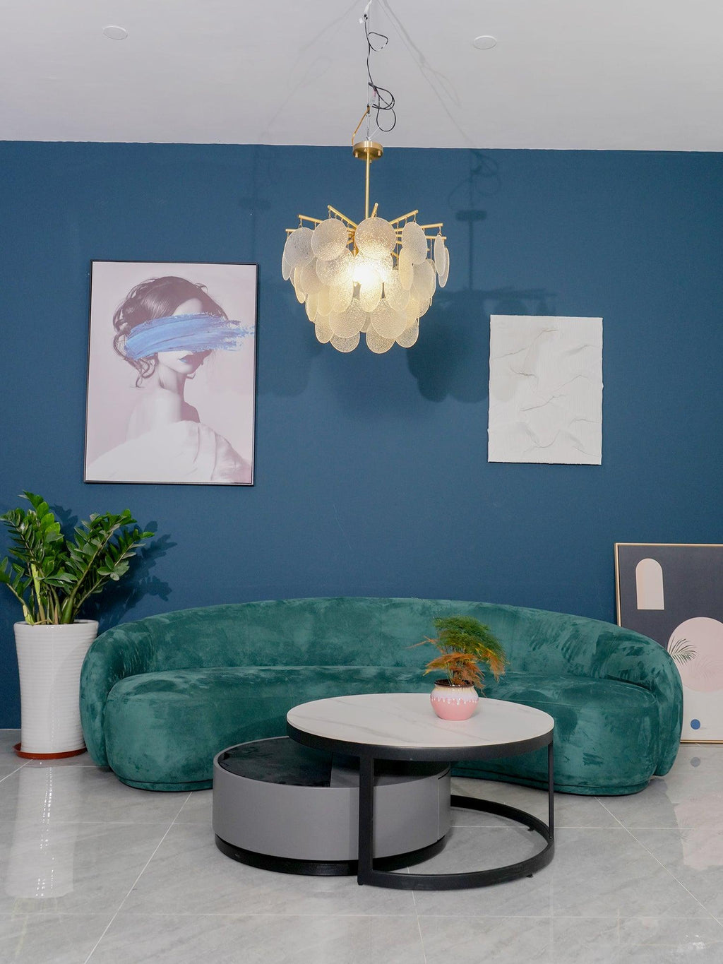 Wide view of a blue lounge with a green curved sofa, a nesting coffee table and this Clérachic disc chandelier overhead.