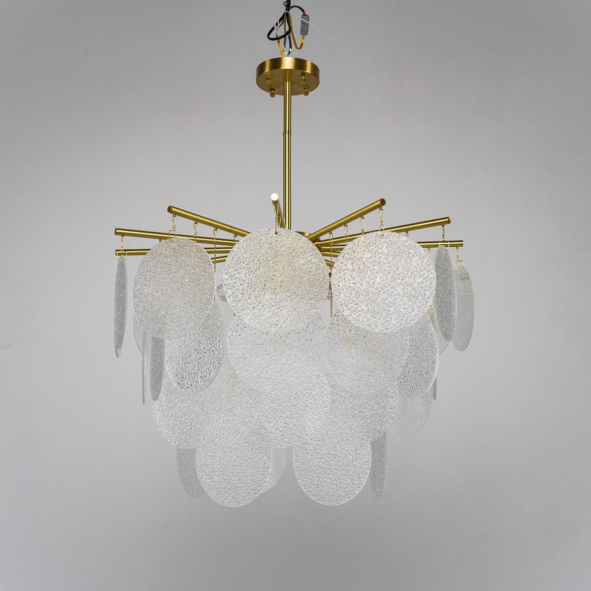 Unlit rippled glass discs and brass arms on this Clérachic chandelier, seen from slightly below against a soft grey backdrop.