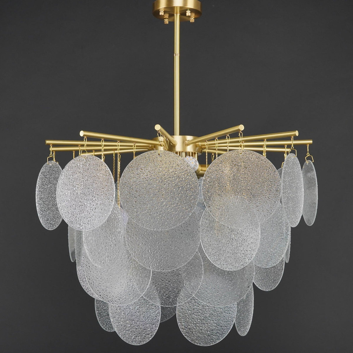 Unlit Clérachic chandelier on a dark grey backdrop, showing the clear, rippled glass discs and the brass-toned arms.