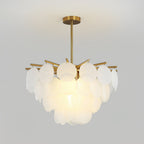 A Clérachic chandelier lit warmly in front of a plain grey backdrop, its frosted discs layered above a brass rod and canopy.
