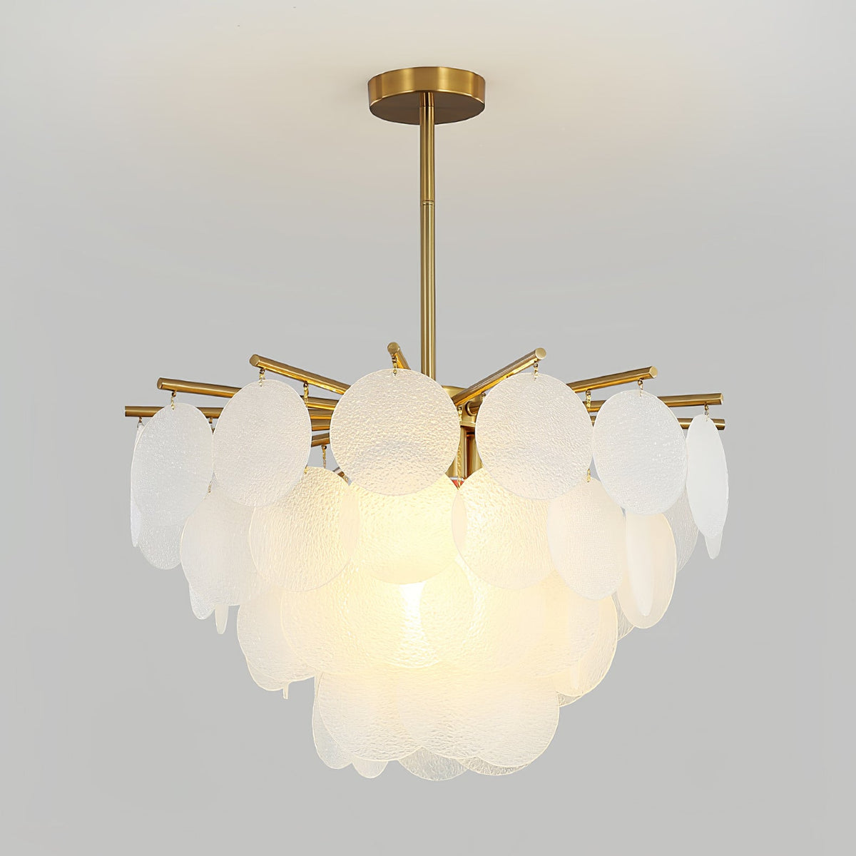 This Clérachic chandelier lit on a grey backdrop, its large frosted discs overlapping in tiers beneath a brass rod.