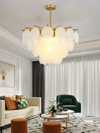 A Clérachic frosted disc chandelier lit above a living room with a cream sofa, a green armchair and a pale curtain.