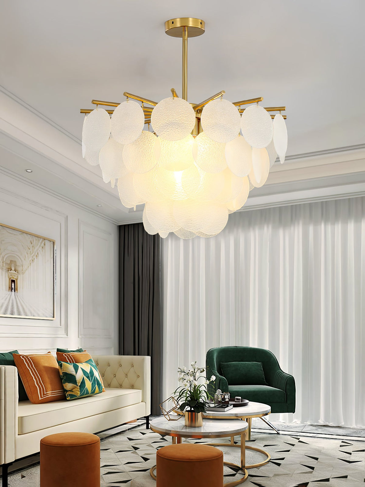 A Clérachic frosted disc chandelier lit above a living room with a cream sofa, a green armchair and a pale curtain.