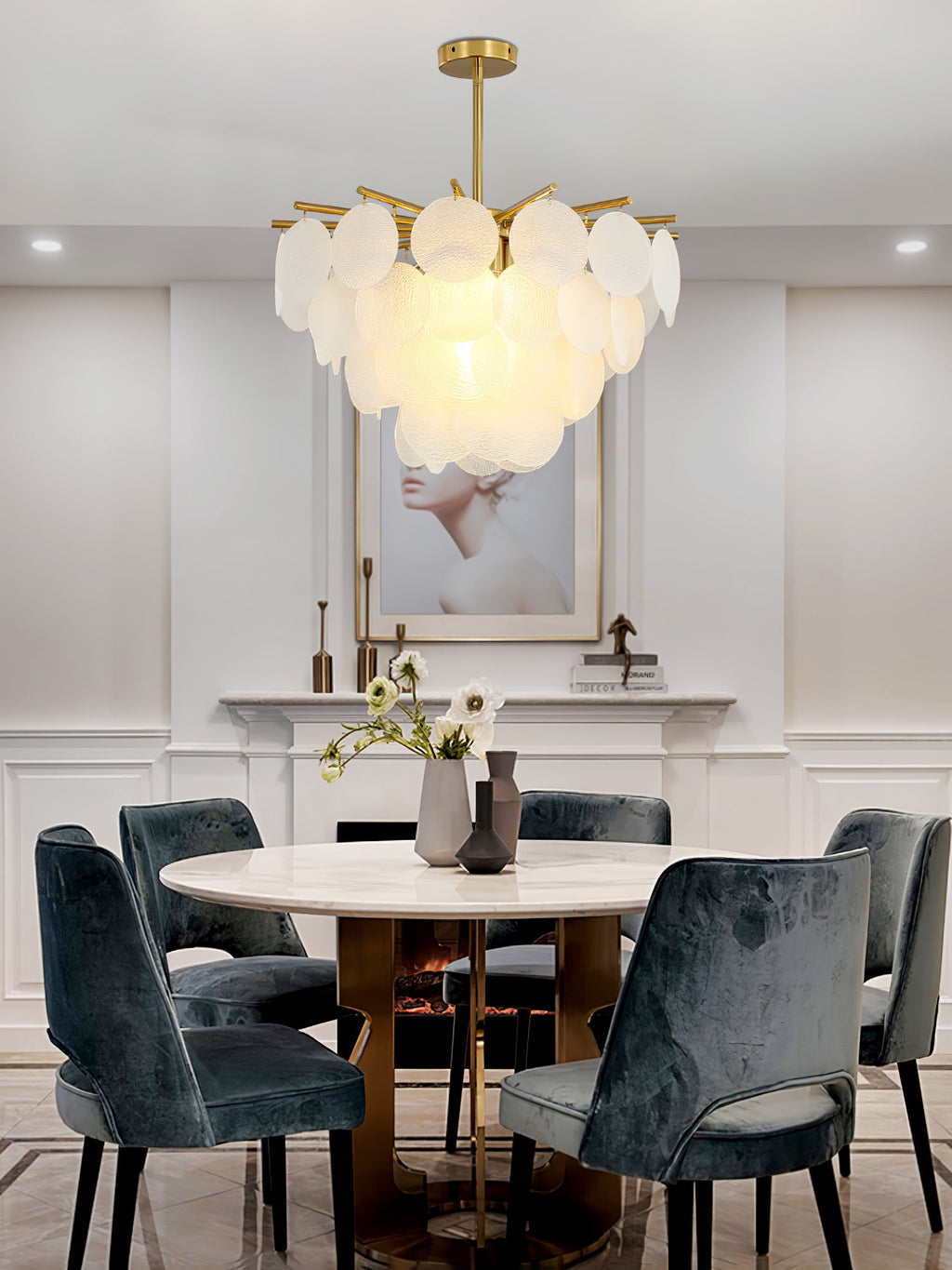 A lit Clérachic chandelier over a round white dining table with teal velvet chairs, in a room with panelled grey walls.