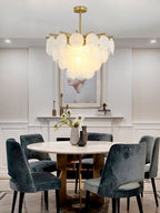 A lit Clérachic chandelier over a round white dining table with teal velvet chairs, in a room with panelled grey walls.