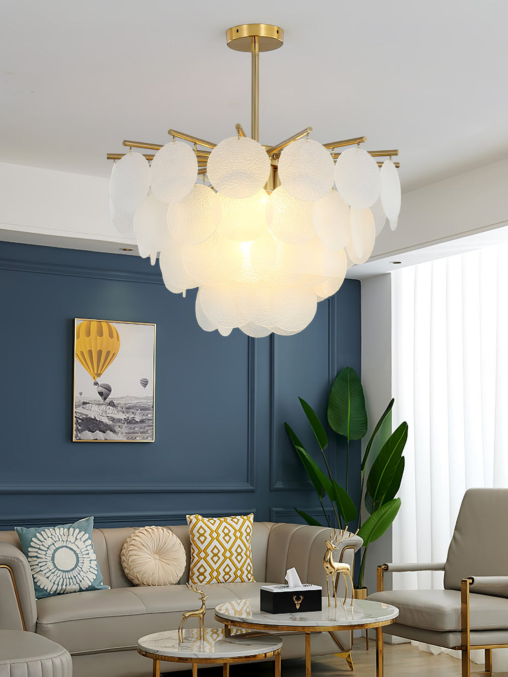 A Clérachic chandelier glowing in a living room with a blue panelled wall, a hot-air balloon print and a beige sofa.