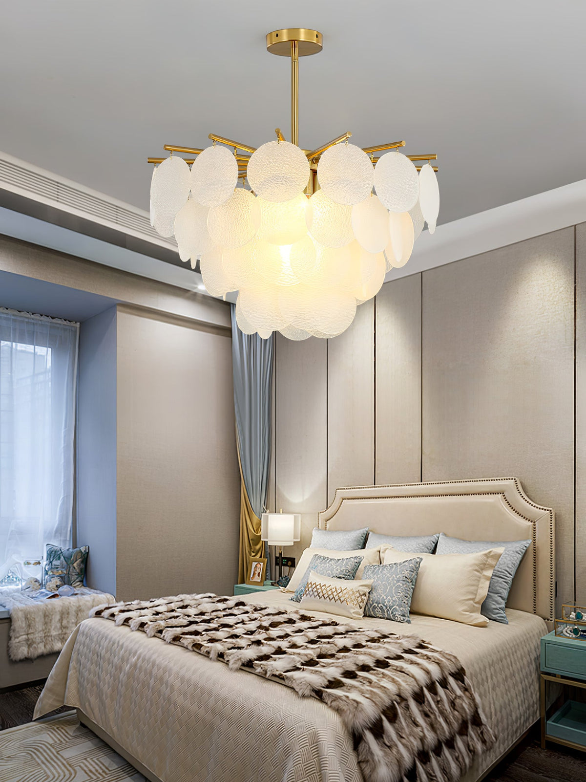 Lit Clérachic frosted disc chandelier hung in a bedroom with a padded headboard, a patterned throw and taupe wall panels.