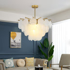 A Clérachic chandelier lit above a living room with a blue panelled wall, a tall plant and a sofa with patterned cushions.