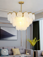 Lit Clérachic chandelier in a living room with a white cornice, patterned cushions on a grey sofa and a vase of yellow flowers.