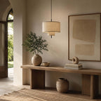 Clérachic pendant hung above a chunky wooden console in a hallway, with a large plant in a vase and a stoneware pot on the floor.