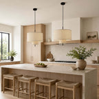 Two Clérachic pendants at different heights over a stone-topped kitchen island lined with woven stools.