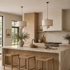 Clérachic linen pendants above a kitchen island with woven-seat stools, black-framed windows and a fruit bowl on the counter.