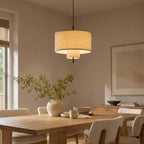 Clérachic pendant seen from a low angle, its linen shade glowing warm over a wooden dining table in a beige room.