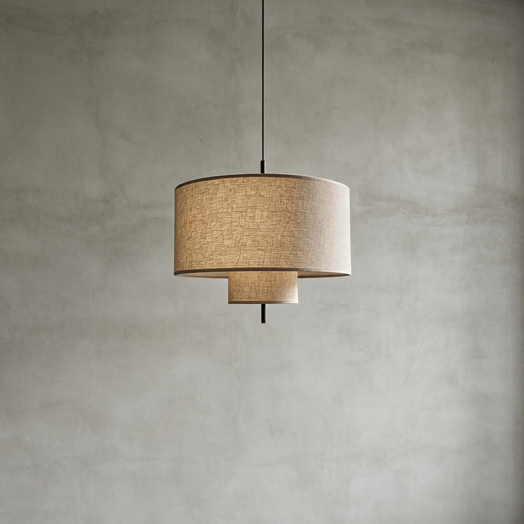 Unlit Clérachic pendant with a natural linen drum shade and a smaller lower tier, hung against a grey concrete-look wall.