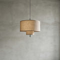 Unlit Clérachic pendant with a natural linen drum shade and a smaller lower tier, hung against a grey concrete-look wall.