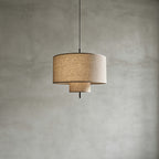 Unlit Clérachic pendant with a natural linen drum shade and a smaller lower tier, hung against a grey concrete-look wall.