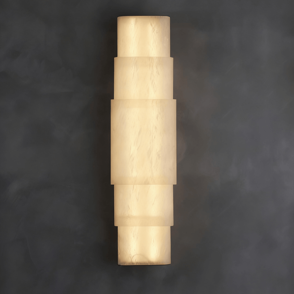 Clérachic tiered alabaster sconce glowing on a dark grey plaster wall, stacked stone bands lit warm.