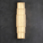 Clérachic tiered alabaster sconce glowing on a dark grey plaster wall, stacked stone bands lit warm.