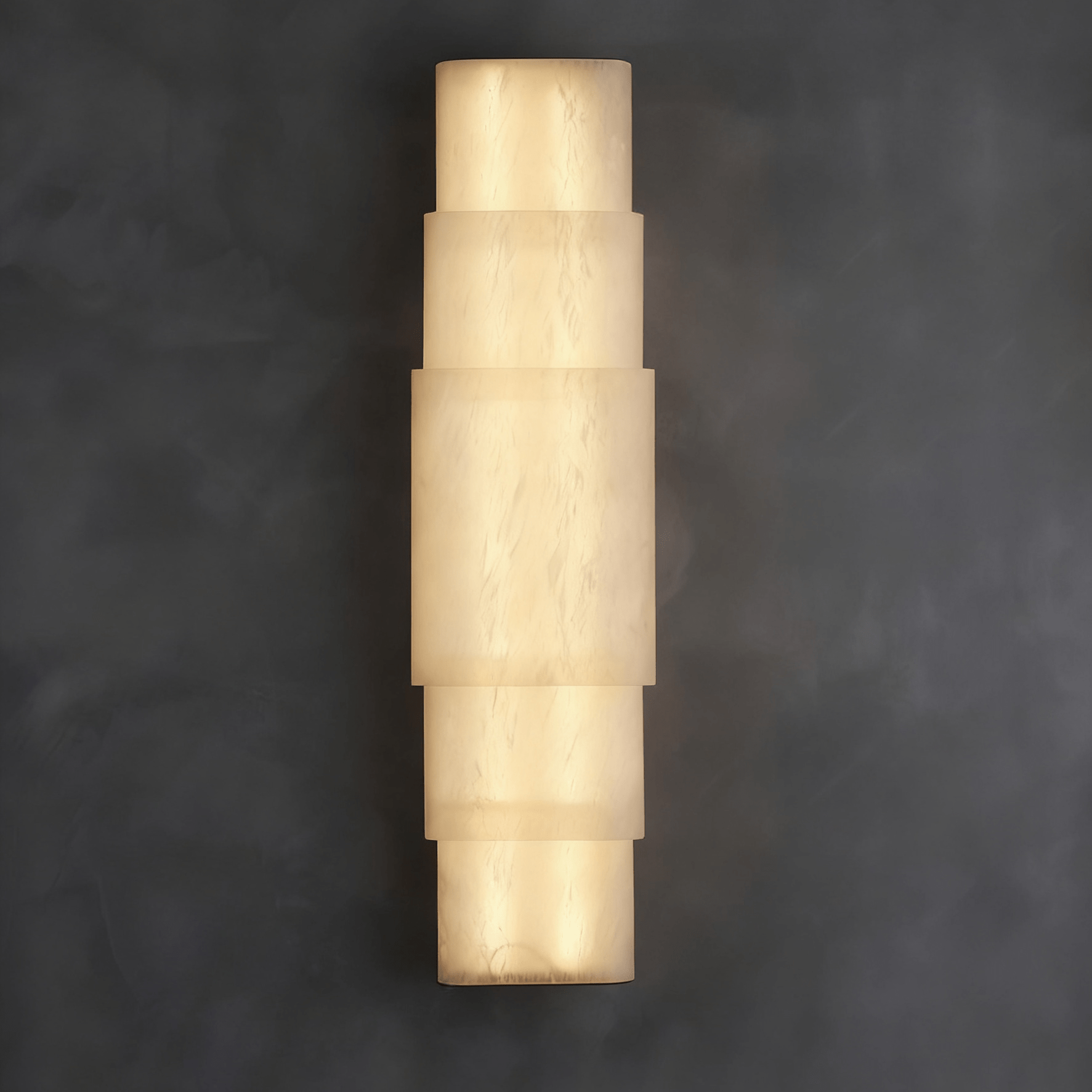 Clérachic tiered alabaster sconce glowing on a dark grey plaster wall, stacked stone bands lit warm.