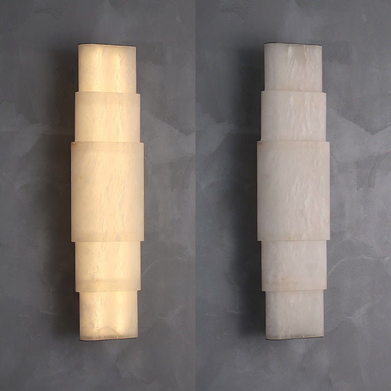 Two sizes of the Clérachic tiered alabaster sconce side by side on grey plaster, one lit, one unlit.
