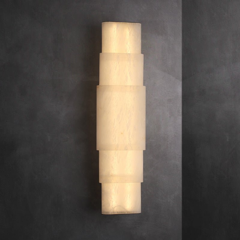 The Clérachic tiered alabaster sconce against charcoal plaster, light spilling from each stone joint.