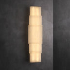The Clérachic tiered alabaster sconce against charcoal plaster, light spilling from each stone joint.