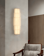 Clérachic tiered alabaster sconce lighting a pale hallway wall beside a timber door and armchair.