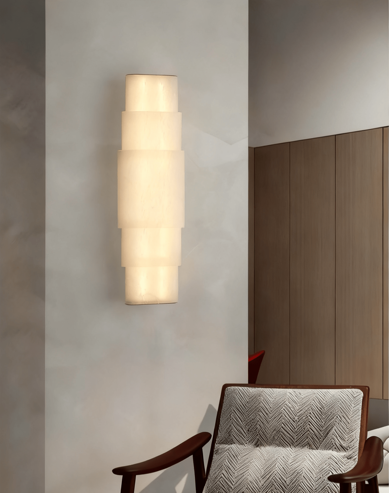Clérachic tiered alabaster sconce lighting a pale hallway wall beside a timber door and armchair.