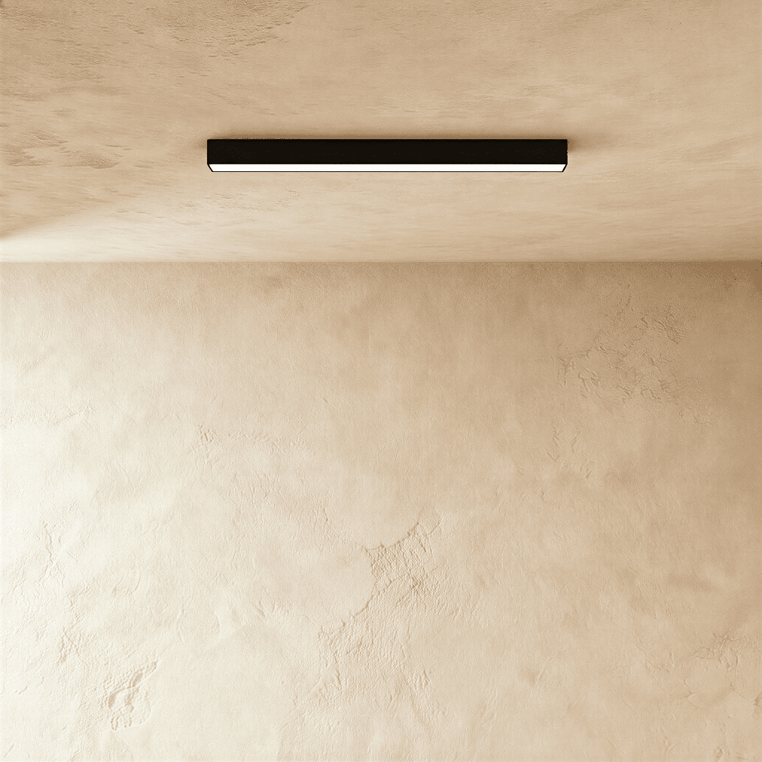 Clérachic linear light head in black, mounted flush to a lime-plastered ceiling with its lit line washing the wall below.