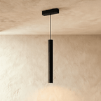 Clérachic cylindrical pendant head in black, lit at its open base and dropping a pool of light on the wall.