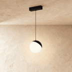 Clérachic globe pendant head in black and white, lit on its cord with a warm glow on the plaster behind.