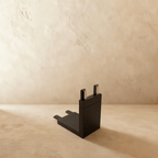 Clérachic track connector in black, an upright right-angle piece with two pin terminals on top, stood on a plaster floor.