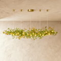 Clérachic's chandelier in its linear form, green glass leaves clustered along a brass branch on rods.
