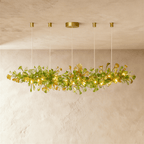 Clérachic's chandelier in its linear form, green glass leaves clustered along a brass branch on rods.
