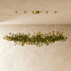 Clérachic's chandelier in its linear form, glowing warm along a spray of green glass leaves overhead.