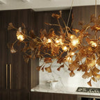 A close detail of the Clérachic chandelier's amber leaves, glowing above a marble island and gas cooktop.